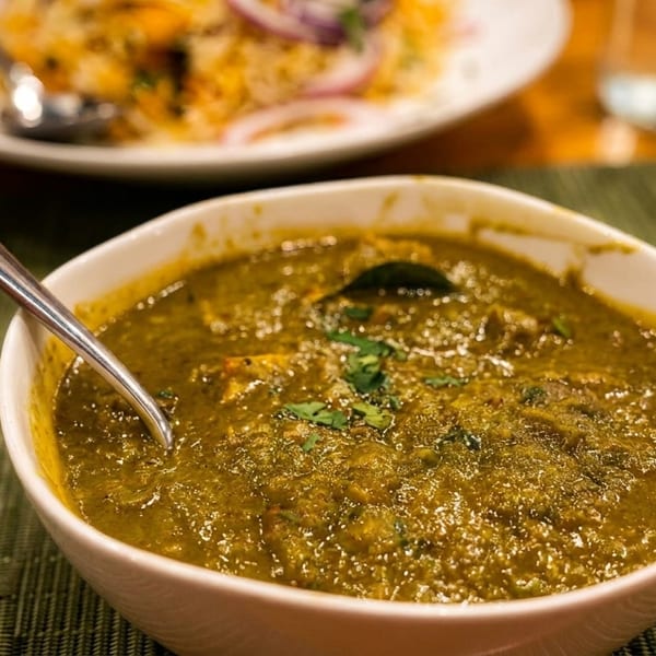 A bowl of green curry with a spoon, garnished with cilantro, on a green placemat.