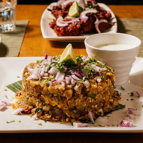 A plate of Indian food with chopped onions, cilantro, and a lime wedge, with a side of raita.