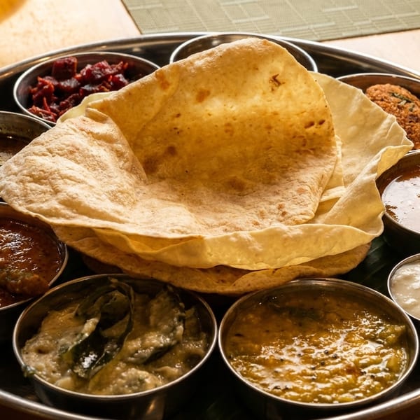 A metal thali platter with various Indian dishes, including curries, flatbread, and chutneys.